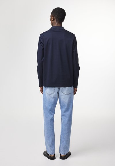 Chemise à manches longues bleu marine avec une coupe droite, associée à un jean droit bleu clair et des chaussures à semelle plate noires.