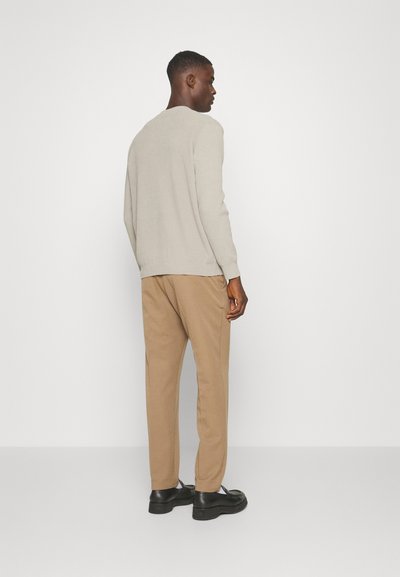 Hellbeiger Pullover, slim fit, weicher Stoff, runder Halsausschnitt. Kombiniert mit hellbraunen Hosen, taillierte Passform, schwarzen Schuhen, minimalistisches Design.