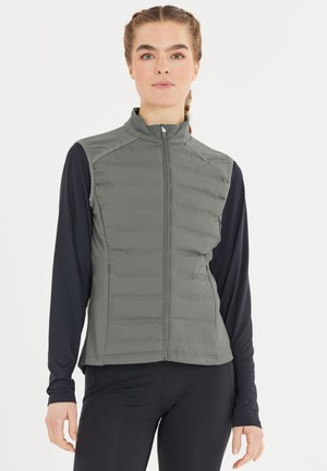Fodrad zip-up väst i olivgrön med hög krage, sidofickor och kontrasterande svarta långärmade tröjor under. Slät textur.