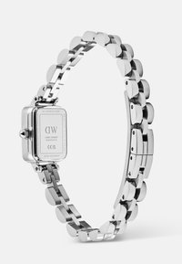 Montre-bracelet en métal argenté avec un boîtier carré, dotée d'une couronne sur le côté et gravée de détails de marque et de numéro de série.