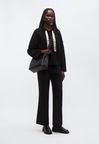 Kvinde iført helt sort outfit med vidde bukser, oversized hættetrøje med hvide snore, sorte støvler, creoløreringe og bærende en sort skuldertaske.