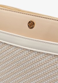 Beżowa pleciona torebka z teksturowanym materiałowym korpusem, kremowymi skórzanymi akcentami, złotym zamkiem błyskawicznym i dekoracyjnym metalowym logo.