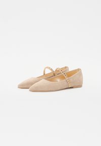 Ballerines en suède beige avec un bout pointu, une sangle élastique ornée de clous dorés et un petit talon. Texture lisse et design minimaliste.