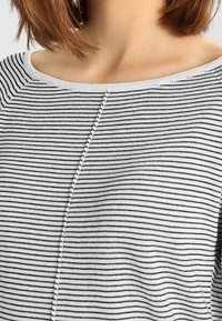 Czarna i biała bluzka w paski z szerokim dekoltem, krótkimi rękawami i teksturowanym materiałem z centralnym przeszyciem.