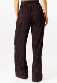Brown, textured wide-leg pants with an elastic waistband, featuring a crinkled design and a smooth finish.