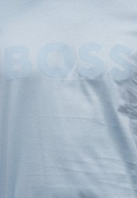 Ανοιχτό μπλε ύφασμα με τη λέξη «BOSS» τυπωμένη σε λίγο πιο σκούρο μπλε χρώμα στην περιοχή του στήθους.