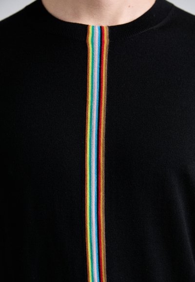 Svart strikkegenser med en sentral vertikal stripe i regnbuefarger, inkludert rød, blå, gul og grønn, nedover fronten.