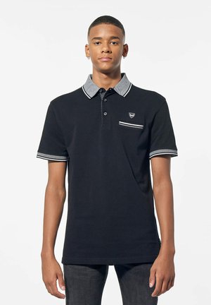 Polo noir avec un col gris et des accents rayés, comportant une poche poitrine et un plastron à trois boutons. Matière en coton avec une texture lisse.