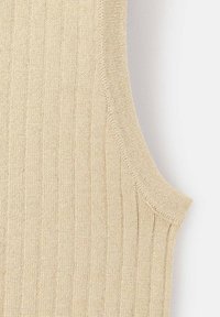 Detailní záběr béžové ribované pletené látky ukazující okraj bezrukávového oděvu a strukturu pletení.