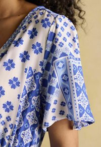 Blau-weißer Stoff mit floralem Muster und geometrischen Designs, mit einem weichen Fall und leichter Textur.