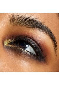 Nærbillede af et øje med mørk eyeliner, gyldent shimmer på øjenlåget og veldefinerede vipper. Hudens struktur er glat med varierede nuancer af brun.