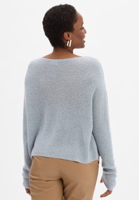 Lichtblauwe gebreide trui met een brede halslijn en lange mouwen. Heeft een geribbelde textuur en een iets losse pasvorm, gecombineerd met beige broek.