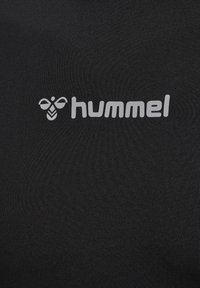 Svart t-shirt med en texturerad tygkvalitet och en slät yta, prydd med en ljusgrå "hummel"-logotyp och ett bi-emblem på vänster sida.