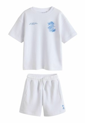 Biała koszulka z krótkim rękawem z niebieskim nadrukiem smoka i napisem Tokyo, w zestawie z białymi szortami na elastycznej gumce, ozdobionymi małymi niebieskimi postaciami.