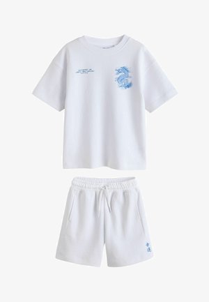 Fehér rövid ujjú póló kék sárkány grafikával és Tokyo felirattal, fehér elasztikus derékpántos rövidnadrággal, amin kis kék figurák találhatók.