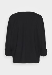 Musta ylikokoinen pusero, jossa pyöreä pääntie, 3/4-hihat ja käännetyt hihansuut. Sileä kangas, minimalistinen muotoilu ilman näkyviä yksityiskohtia.