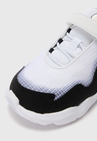 Hvit og svart treningsto wearing med teksturert mesh-overdel, polstret krage og justerbar stropp, med slitesterk gummisåle og elegante linjer.
