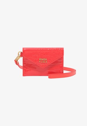 Błyszczący, jasny różowy portfel na karty z lakierowanej skóry tłoczonej w wzór krokodyla, z detalem złotego logo i odpinanym paskiem na nadgarstek. Smukły, prostokątny kształt.