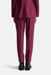 Abito tailleur bordeaux con pantaloni a gamba dritta. Tessuto liscio e strutturato. Stivali neri con suola spessa completano l'outfit.