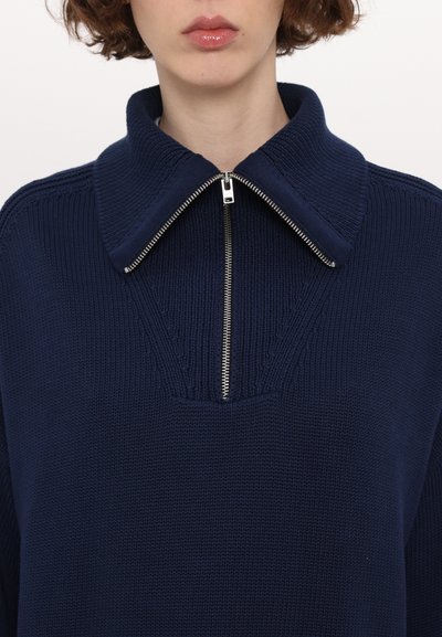 Mørkeblå strikket sweater med en stor krave og sølv lynlås, med et tekstureret mønster og en afslappet pasform.