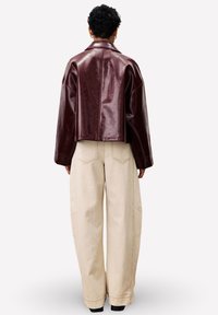 Bordeaux kunstlederen cropped jack met een gelapte kraag, gecombineerd met losse beige broeken met zichtbare stiksels en zijzakken.