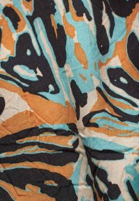 Flerfärgad tyg med abstrakta mönster i svart, turkos och orange. Texturen verkar något vävd och strukturerad.