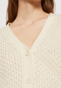 Krämfärgad stickad cardigan med V-ringning, strukturerat mönster, två framknappar och ribbade kanter.