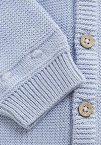 Ljusblå stickad kofta med ett texturerat mönster, ribbade muddarna och träknappar med en stjärna i centrum.