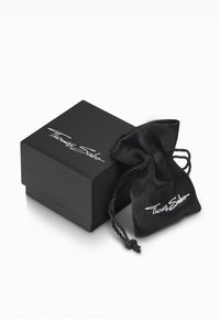 Scatola regalo nera con una finitura liscia, caratterizzata da un logo bianco, e un sacchetto di satin nero abbinato con chiusura con cordoncino accanto.