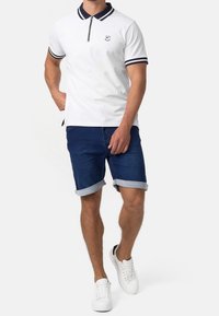 Polo blanc à fermeture éclair avec un col rayé bleu marine, associé à un short en denim bleu foncé retroussé et des baskets blanches.