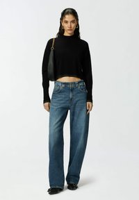 Crni skraćeni pulover, traperice visoko struk, širokih nogavica u plavoj boji, te crna torba s lancem. Glatka tekstura, ležeran kroj.