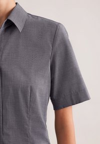 Maglietta a maniche corte di colore grigio scuro con tessuto strutturato. Presenta un colletto appuntito e un design aderente con cuciture verticali.