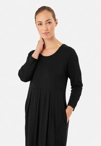 Abito lungo nero a maniche lunghe con scollatura rotonda, con un fondo plissè e tasche laterali, realizzato in tessuto morbido.