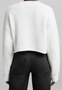 Pull blanc tricoté court avec texture côtelée et coupe ample, assorti à un jean en denim noir taille haute avec poches arrière.