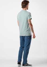 Ljusgrön kortärmad t-shirt med rund halsringning, matchad med blå jeans och svarta sneakers, sedd bakifrån.