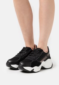 Svarta sneakers som har en kombination av tyg och mocka, med en vit sula. "Armani Emporio"-logotyp i metalliskt silver på sidan.