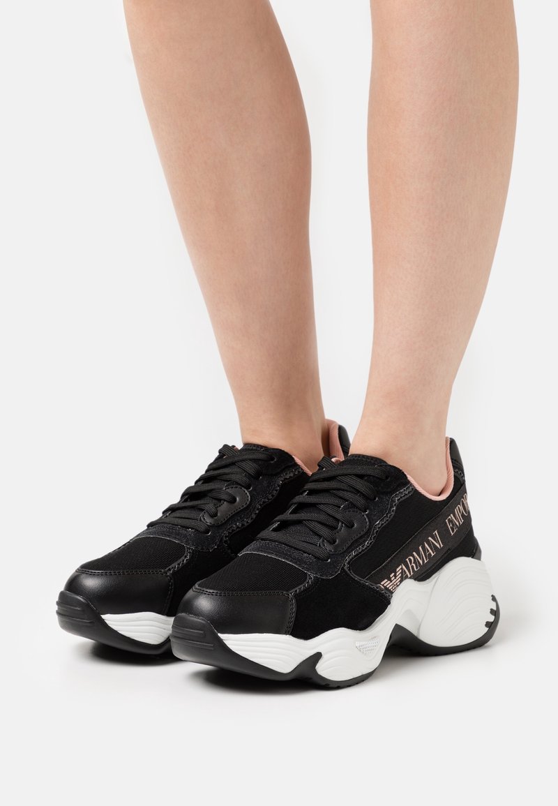 Svarta sneakers som har en kombination av tyg och mocka, med en vit sula. "Armani Emporio"-logotyp i metalliskt silver på sidan.