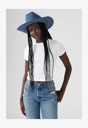 Weißes, kurzärmliges, eng anliegendes T-Shirt kombiniert mit hellblauen, ausgewaschenen, hoch-taillierten Jeans und einem breitrandigen Denim-Hut.