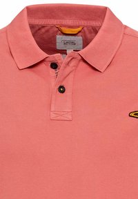 Licht koraalkleurig polo shirt van een textuurstof, met twee zwarte knopen bij de kraag en een gele accentlus aan de achterkant. Bevat een logo op de borst.