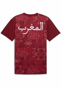 قميص رياضي أحمر يتميز بتصميم مخطط بنمط هندسي. كلمة "المغرب" مطبوعة باللون الأبيض على الجزء العلوي من الظهر. بأكمام قصيرة.