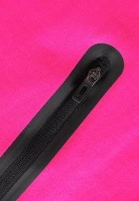 Tessuto fucsia con una texture liscia, caratterizzato da una zip nera lungo un bordo, fissata da una striscia di tessuto nero sottile.