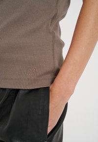 Brązowy prążkowany top na ramiączkach z małym logo na dolnym brzegu, w zestawie z czarnymi skórzanymi spodniami. Charakteryzuje się dopasowanym krojem oraz delikatnym wykończeniem szwów.