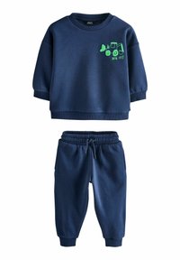 Tumesinine dressipluus rohelise ekskavaatori graafikuga rinnal, koos sobivate jookspükstega, millel on elastne vöökoht.