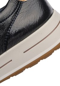 Black shiny leather sneaker heel with white textured midsole and brown rubber outsole, showing detailed stitching and surface texture.