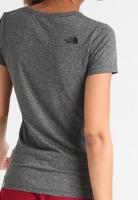 Szary t-shirt z krótkim rękawem wykonany z miękkiego materiału. Posiada okrągły dekolt i małe czarne logo na górnej części pleców. Gładka faktura.