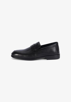Mocassin pour homme en cuir noir avec un petit talon, un bout arrondi et une lanière sur le dessus, présenté sur un fond blanc.