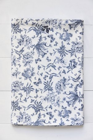 Model floral în tonuri de albastru pe un fundal alb, cu diverse fluturi și flori, având un monogram mic în colțul de sus.