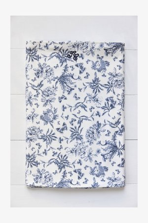 Motivo floreale su tessuto in tonalità blu su fondo bianco, con varie farfalle e fiori, e un piccolo monogramma nell'angolo superiore.