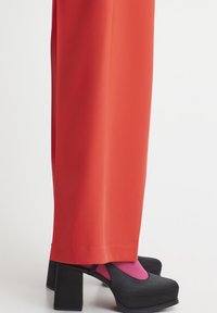 Black platform shoes with a wide heel, paired with bright pink socks. The outfit features loose, orange pants with a smooth texture.