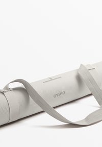 Siva joga matica iz teksturiranega materiala, vključuje trak za prenašanje, prikazuje subtilen logo in minimalističen dizajn.